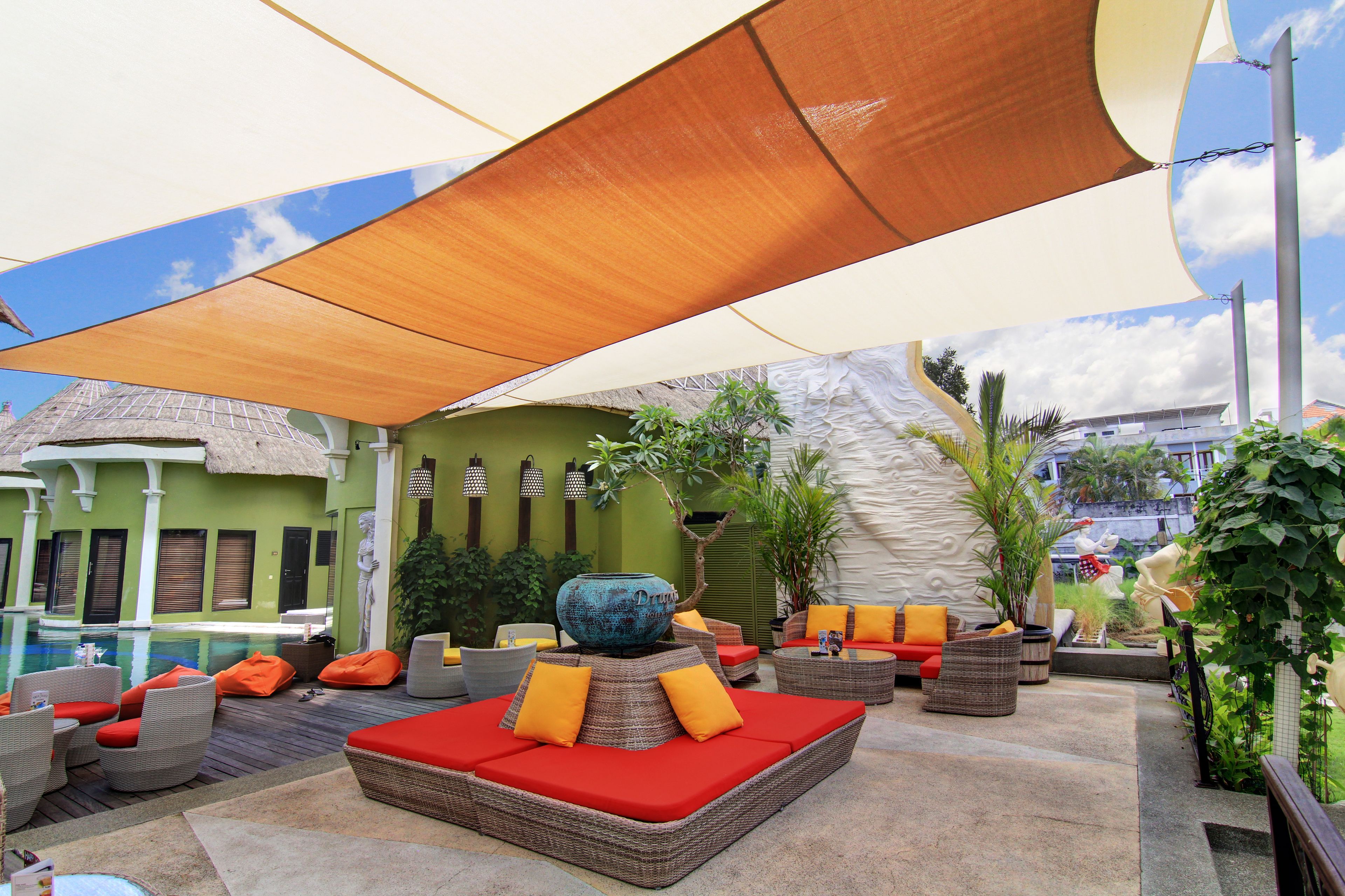 Un espace aménagé au bord de la piscine, avec des meubles en osier, un grand vase décoratif et, au fond, un bâtiment dont le toit est recouvert de chaume.