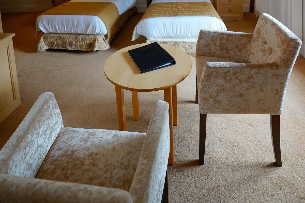 A cozy attic bedroom with two beds, a small table, and two armchairs.