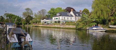 A riverside property with a large house, docked boats, and lush greenery.