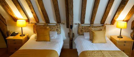 A room with two beds, wooden beams on the ceiling, bedside lamps, and a telephone on the nightstand.