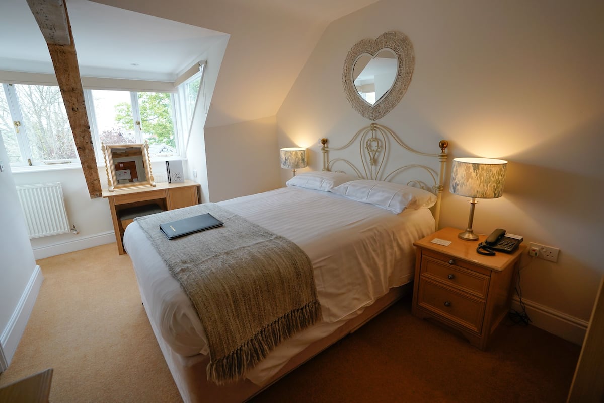 A bedroom with a bed, bedside lamps, a nightstand, a mirror, and a window with a view.
