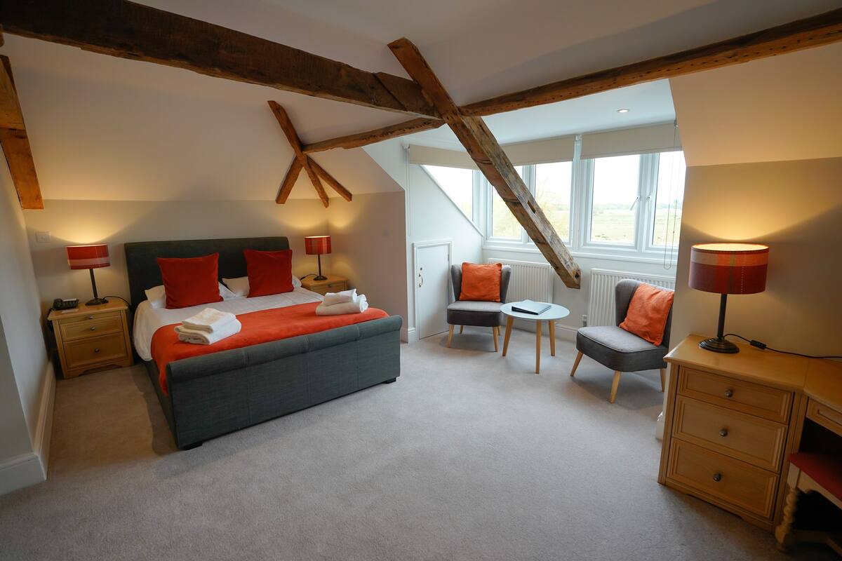 A bedroom with a large bed, a chair, a small table, and a dresser.