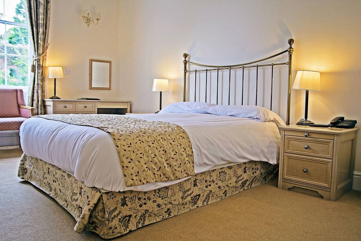 A neatly made bed with a patterned bedspread, a bedside table with a lamp, and a nightstand with a phone.
