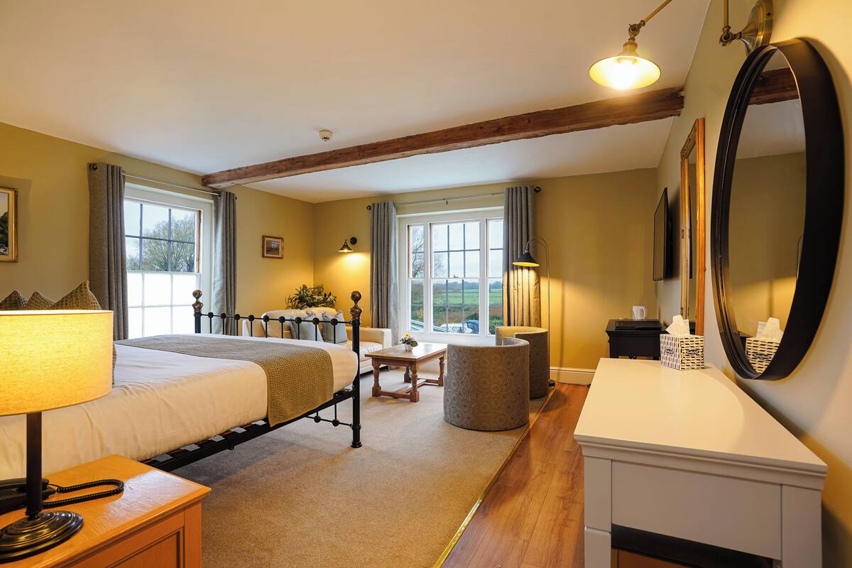A well-lit bedroom with a bed, bedside table, lamp, and a large mirror.