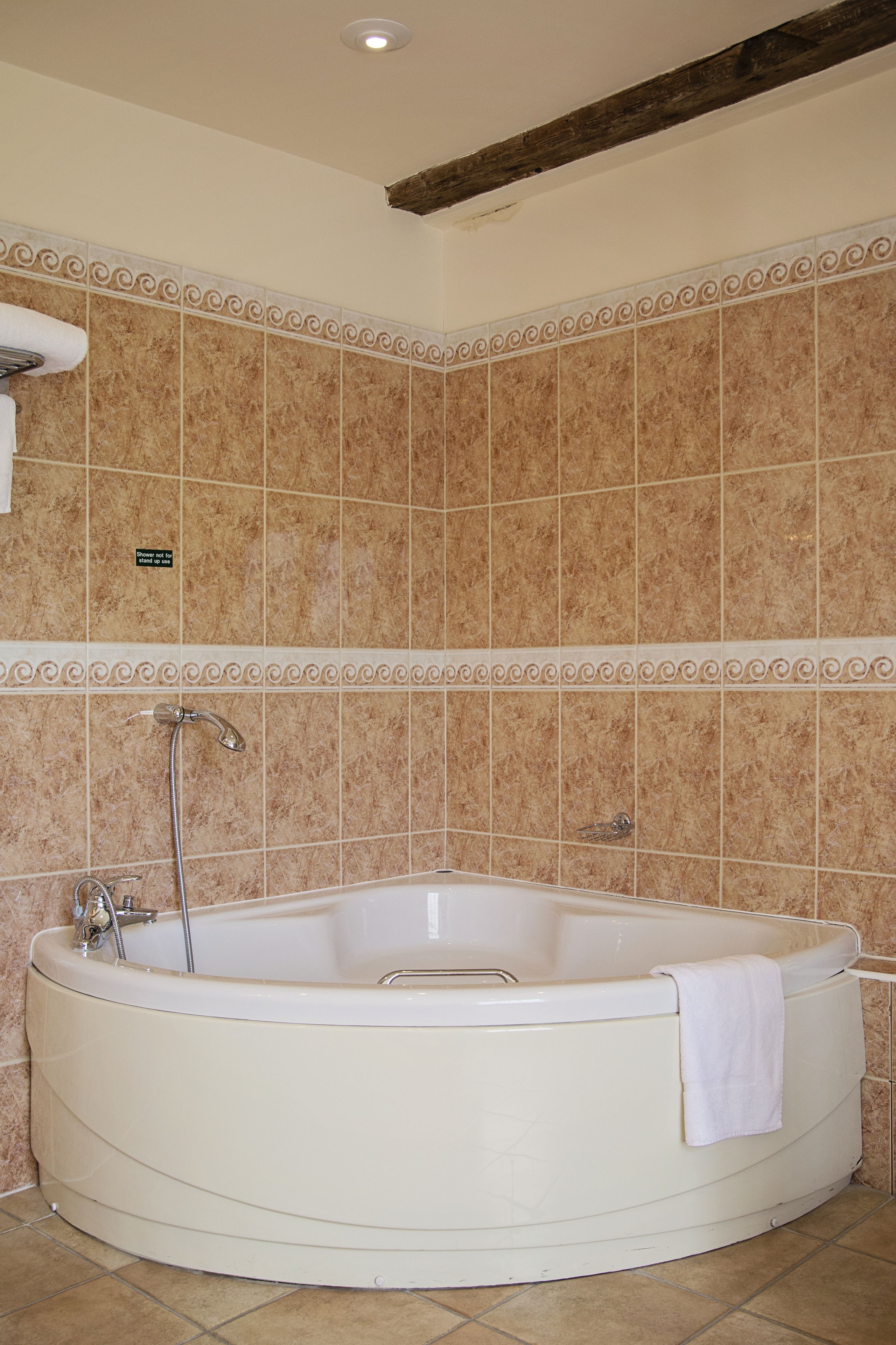 Eine große, freistehende Badewanne in einem Badezimmer mit beige gefliesten Wänden und einer dekorativen Bordüre.