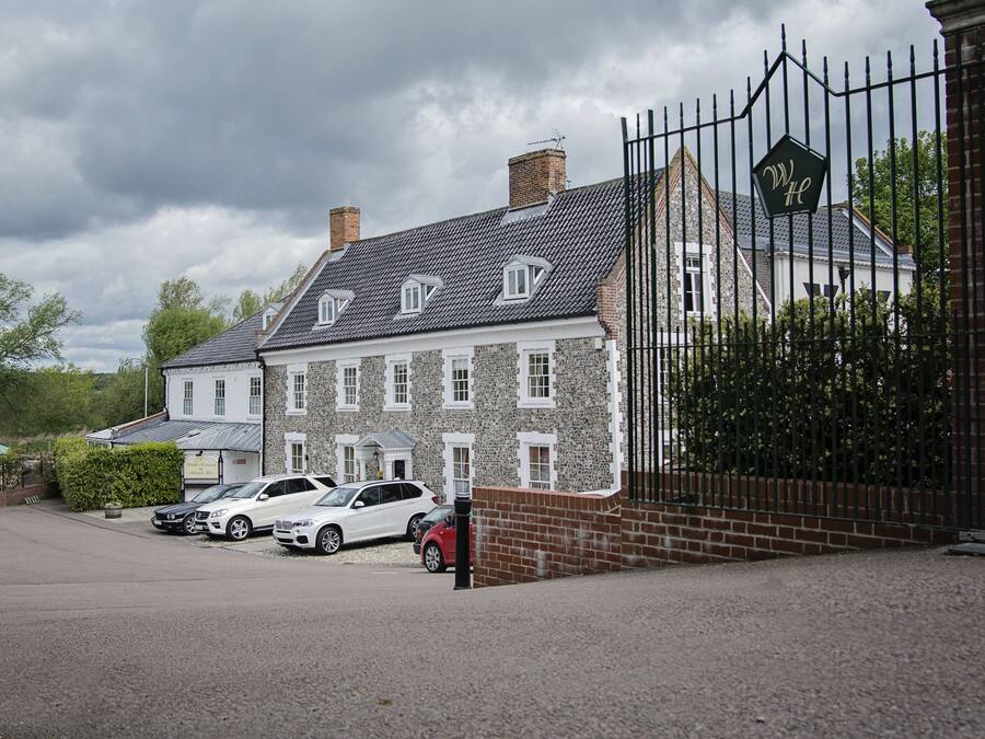 A large stone building with a gated entrance, several parked cars, and a cloudy sky.