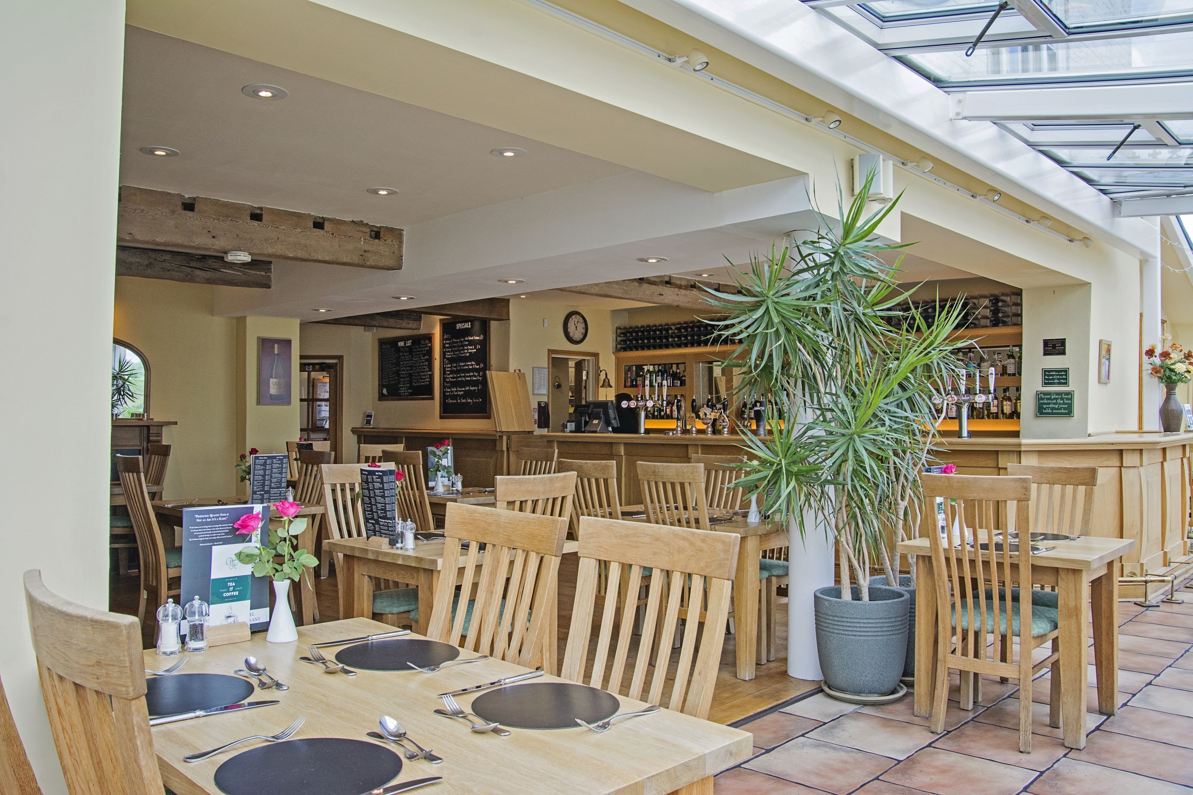 Un restaurant avec des tables et des chaises en bois, un coin bar et une grande plante en pot.
