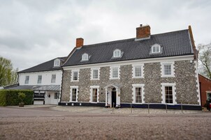 Un bâtiment en pierre de deux étages, avec un toit d’ardoise, une entrée centrale dotée d’un petit porche et une enseigne indiquant « Riverside ».