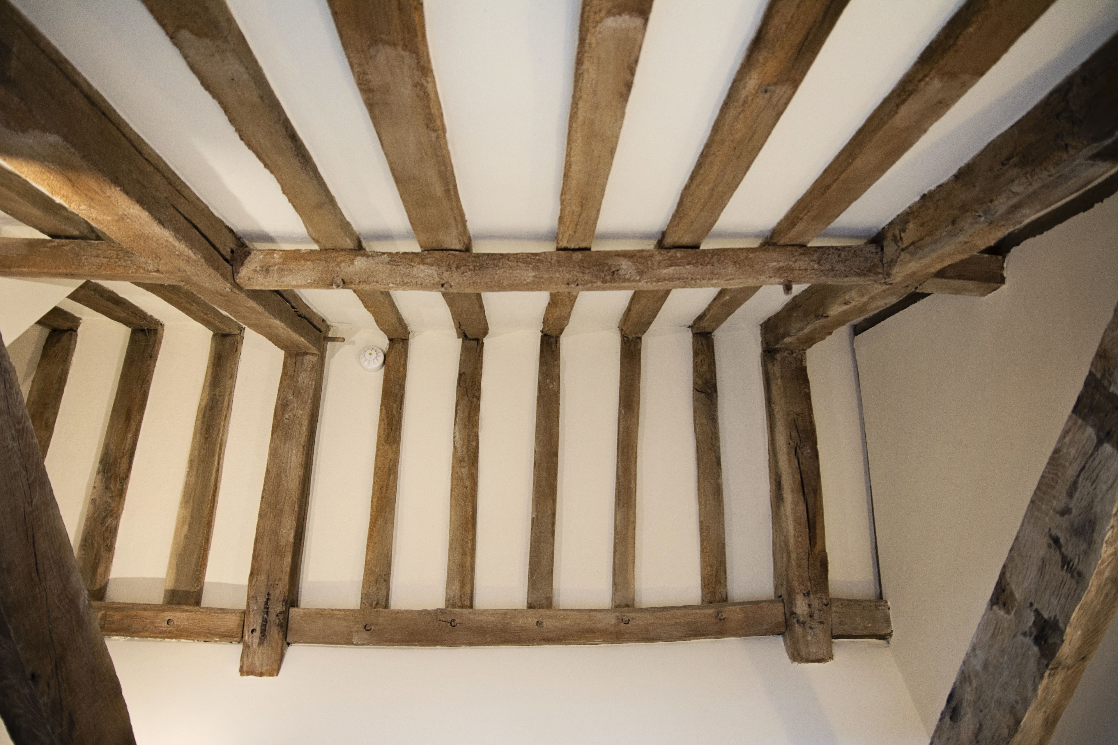 A ceiling with exposed wooden beams and a white wall.