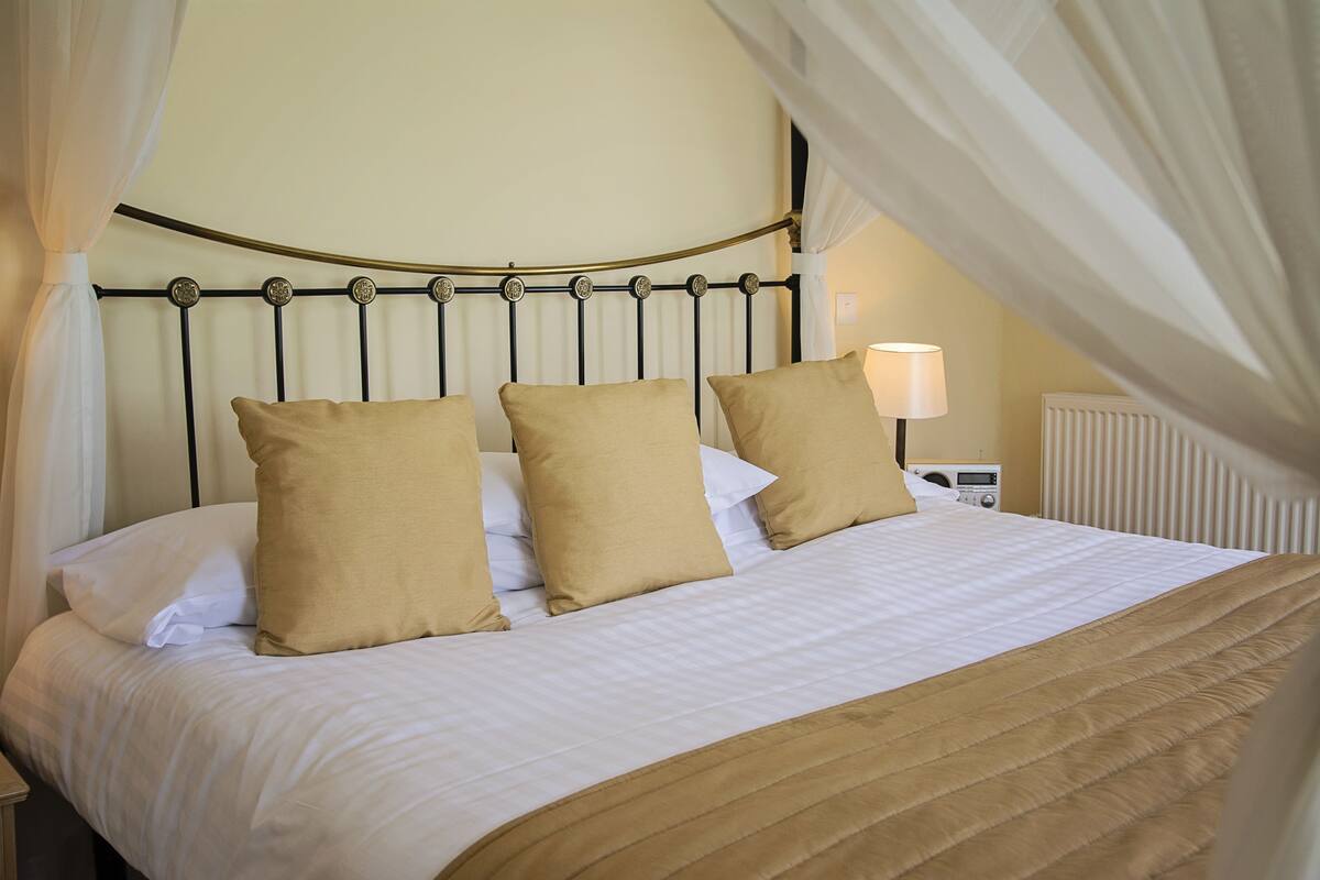 A bed with a canopy, white bedding, and three beige pillows.