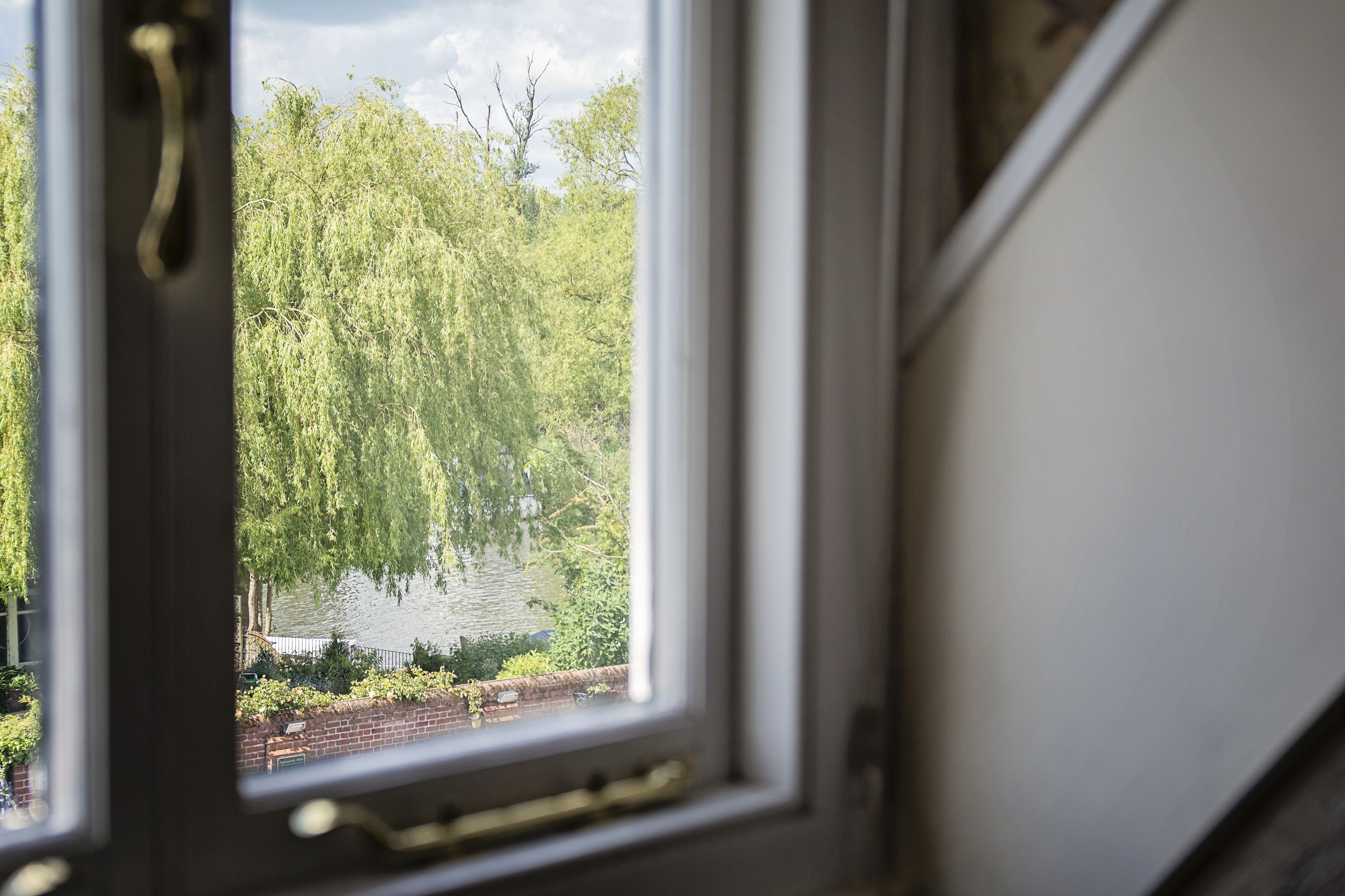 A view through a window of a river with trees and a brick wall.