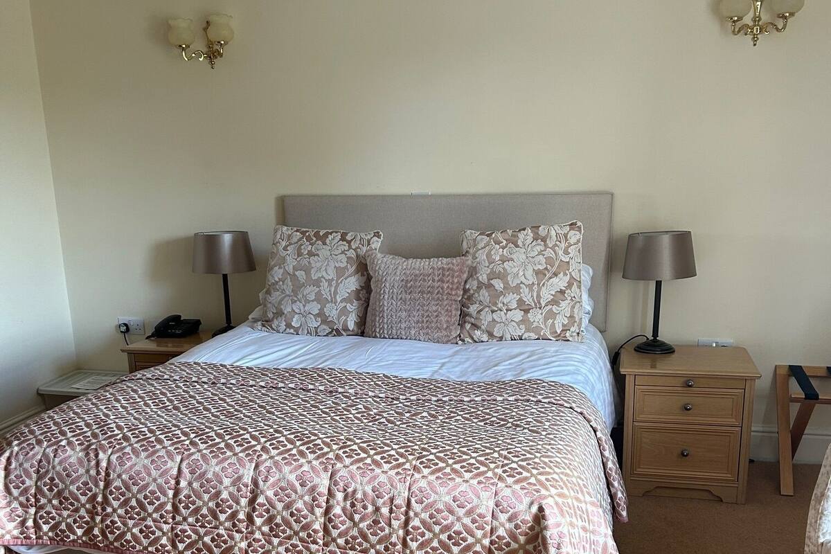 A neatly made bed with patterned bedding, two bedside tables with lamps, and a wall-mounted light fixture.