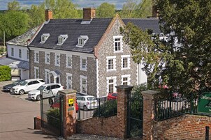 Un bâtiment traditionnel en pierre, doté d’un toit à deux versants et de nombreuses fenêtres, entouré d’un parking où sont garées plusieurs voitures.