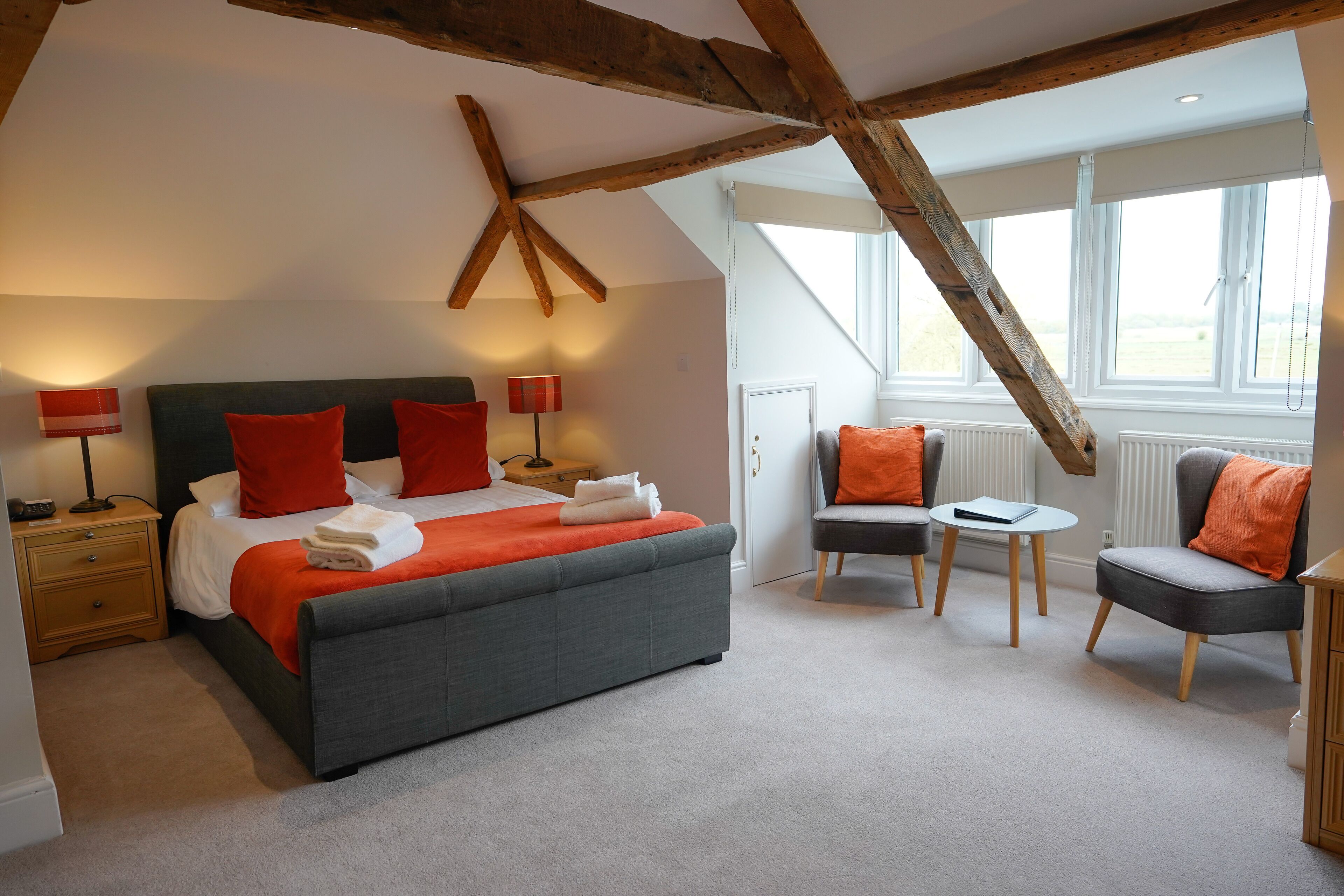 A bedroom with a large bed, two nightstands, a chair, a small table, and a window with a view.