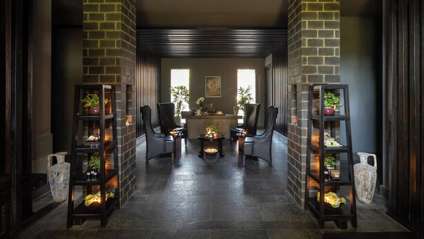 A reception area with a reception desk, two chairs, a coffee table, and two shelving units with plants. - Anantara Mui Ne Resort (Mui Ne)