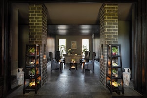 A reception area with a reception desk, two chairs, a coffee table, and two shelving units with plants.