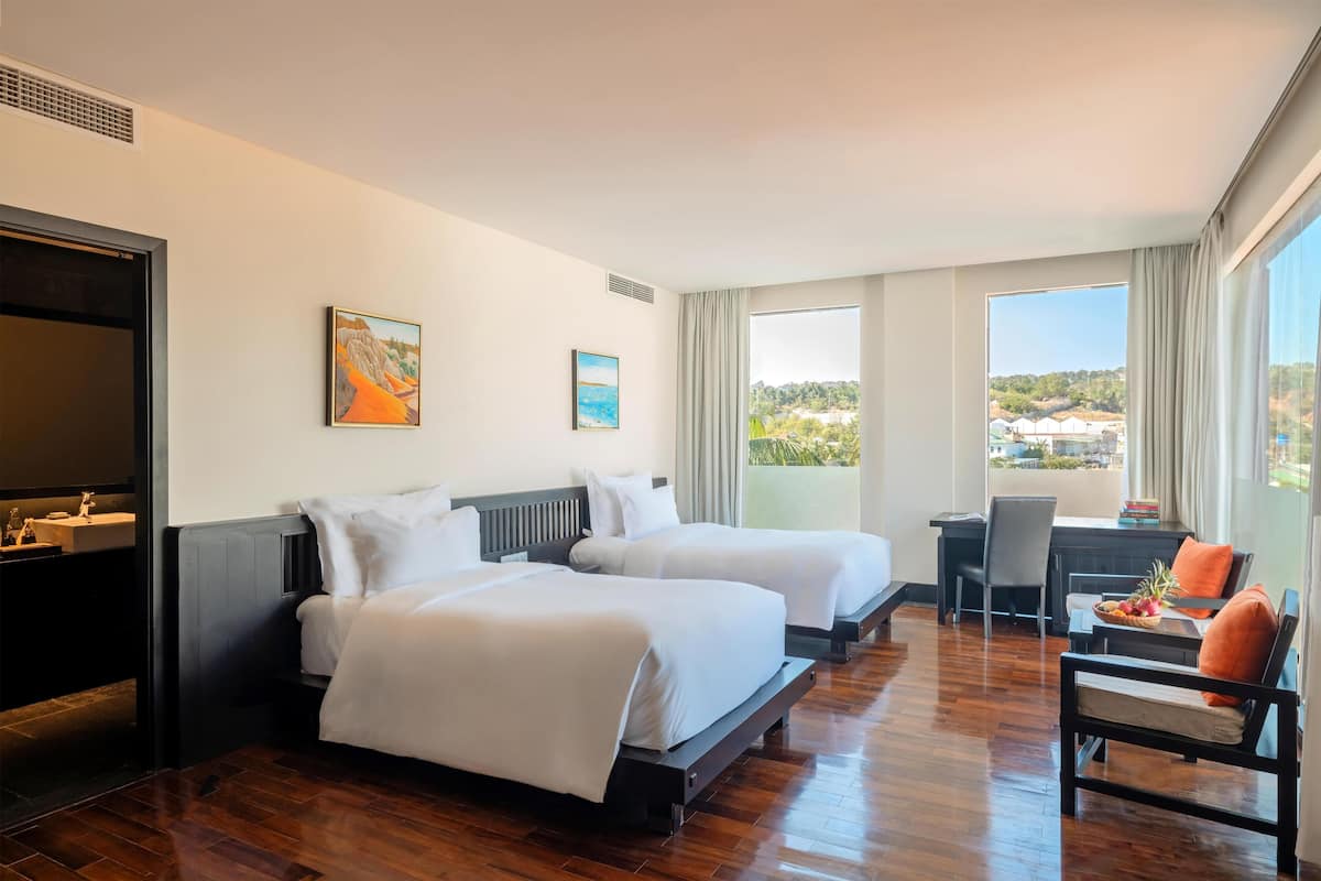 A hotel room with two beds, a desk, a chair, and a view of the landscape.