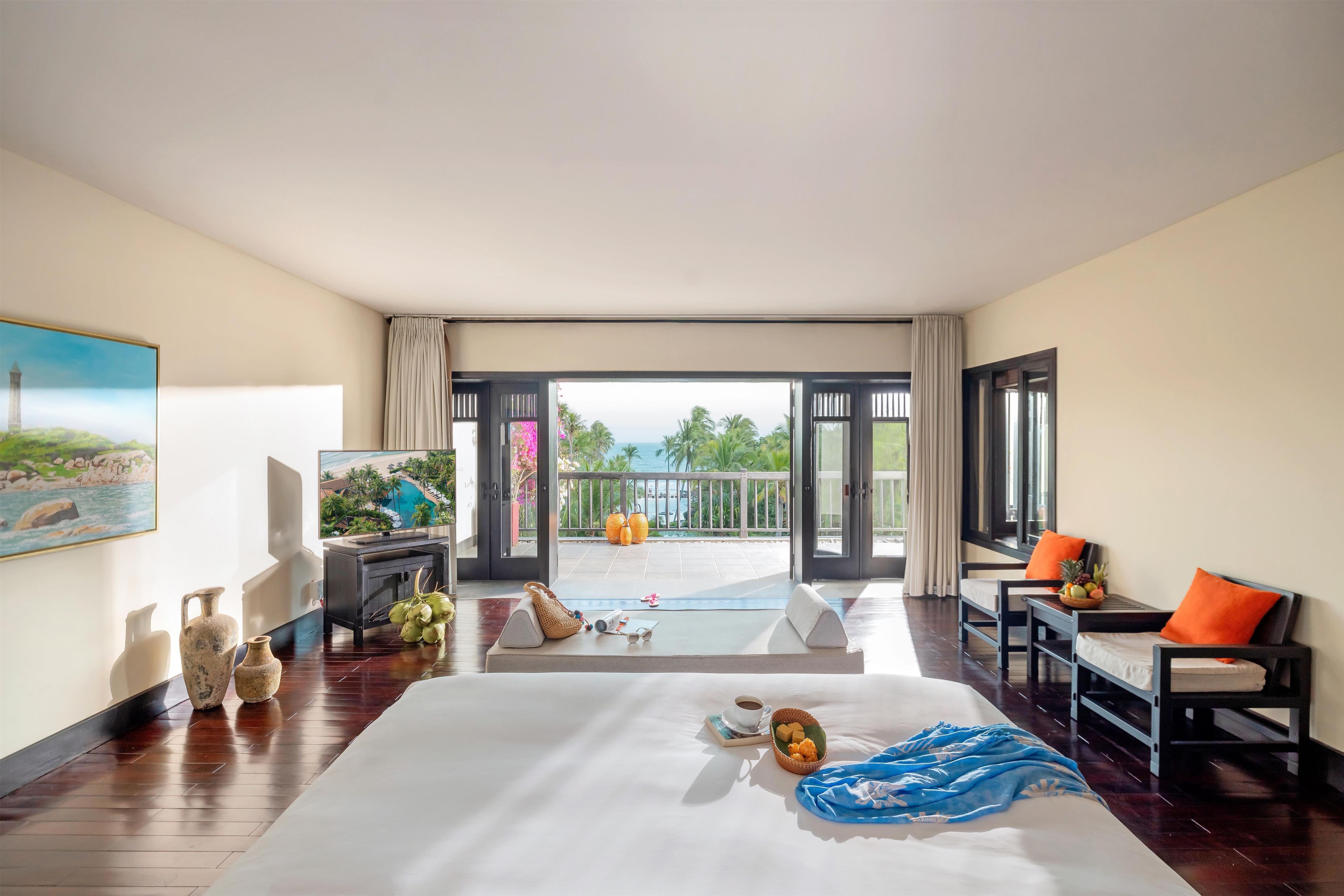 A hotel room with a bed, a desk, a chair, a balcony with a view, and a painting on the wall.