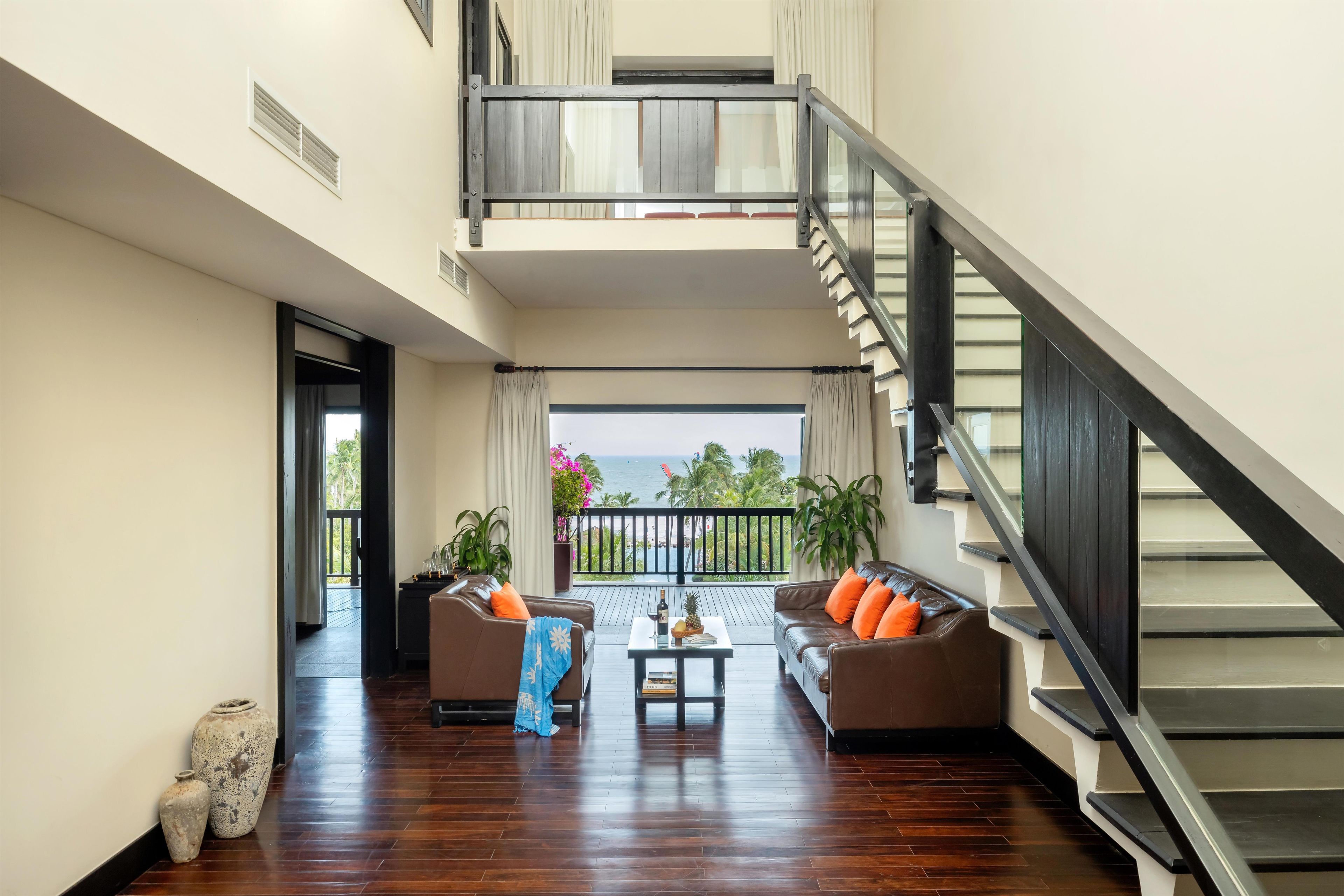 A spacious living area with a wooden floor, a staircase, and a balcony with a view of the sea.