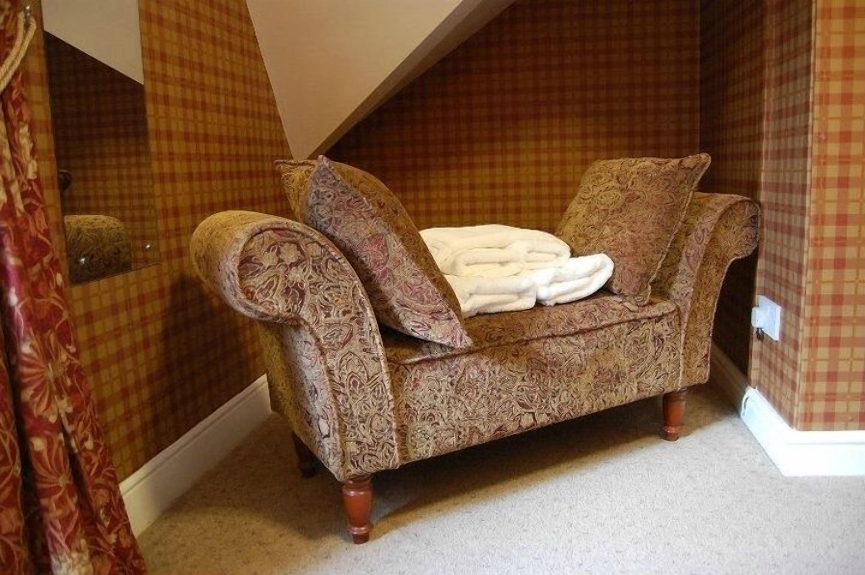 Quarto nos fundos com uma confortável sofa-cama estampada, um espelho e papel de parede quadriculado.