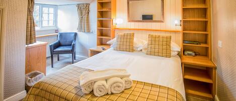 Une chambre d’hôtel avec un lit, une chaise, une table de chevet, une bibliothèque et une fenêtre avec des rideaux.