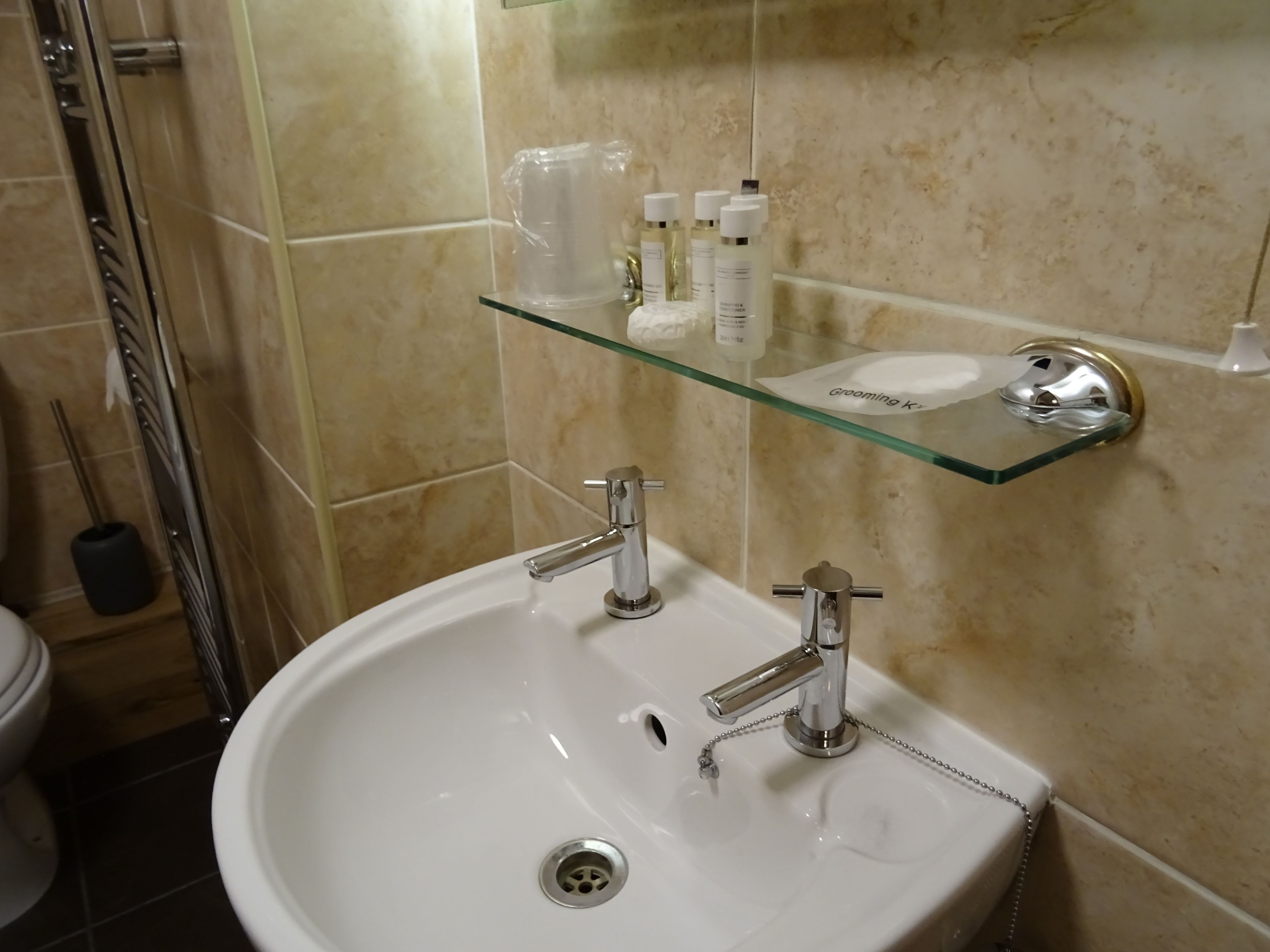 A bathroom with a white sink, a glass shelf with toiletries, and a shower area.