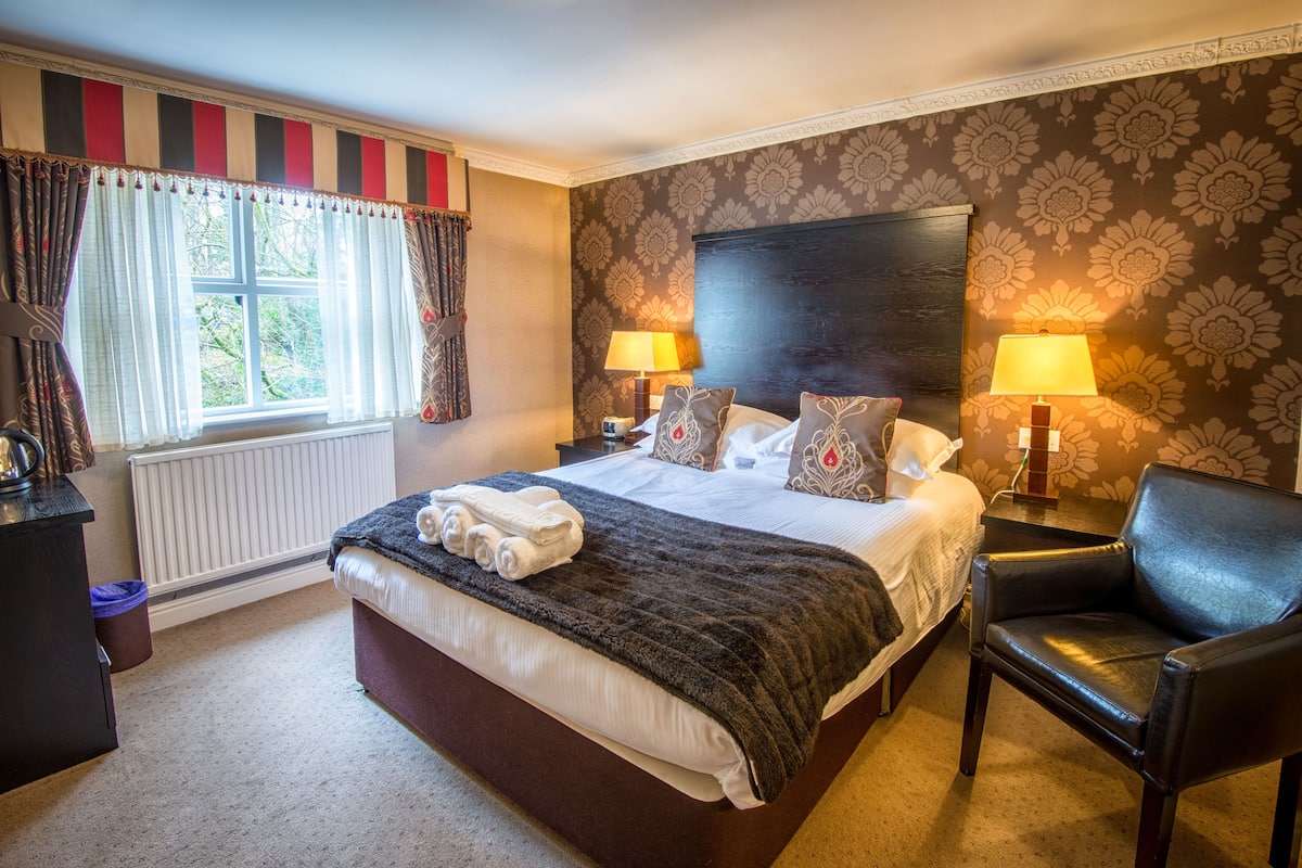 A hotel room with a large bed, two bedside lamps, a chair, and a window with curtains.