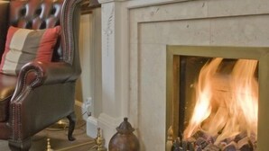 A traditional living room with a fireplace, a leather armchair, and classic decor. - Woodlands Guest House Windermere (Windermere)