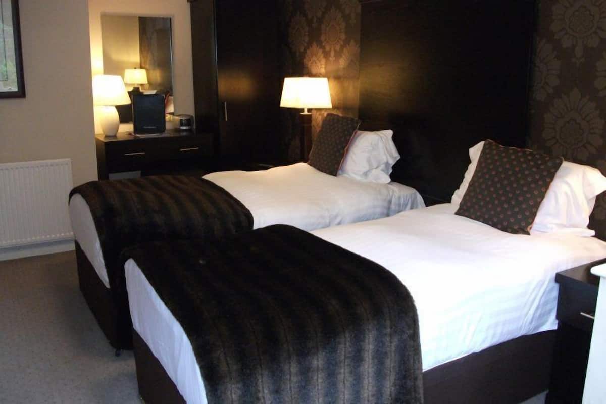 A hotel room with two beds, a nightstand with a lamp, and a dresser.