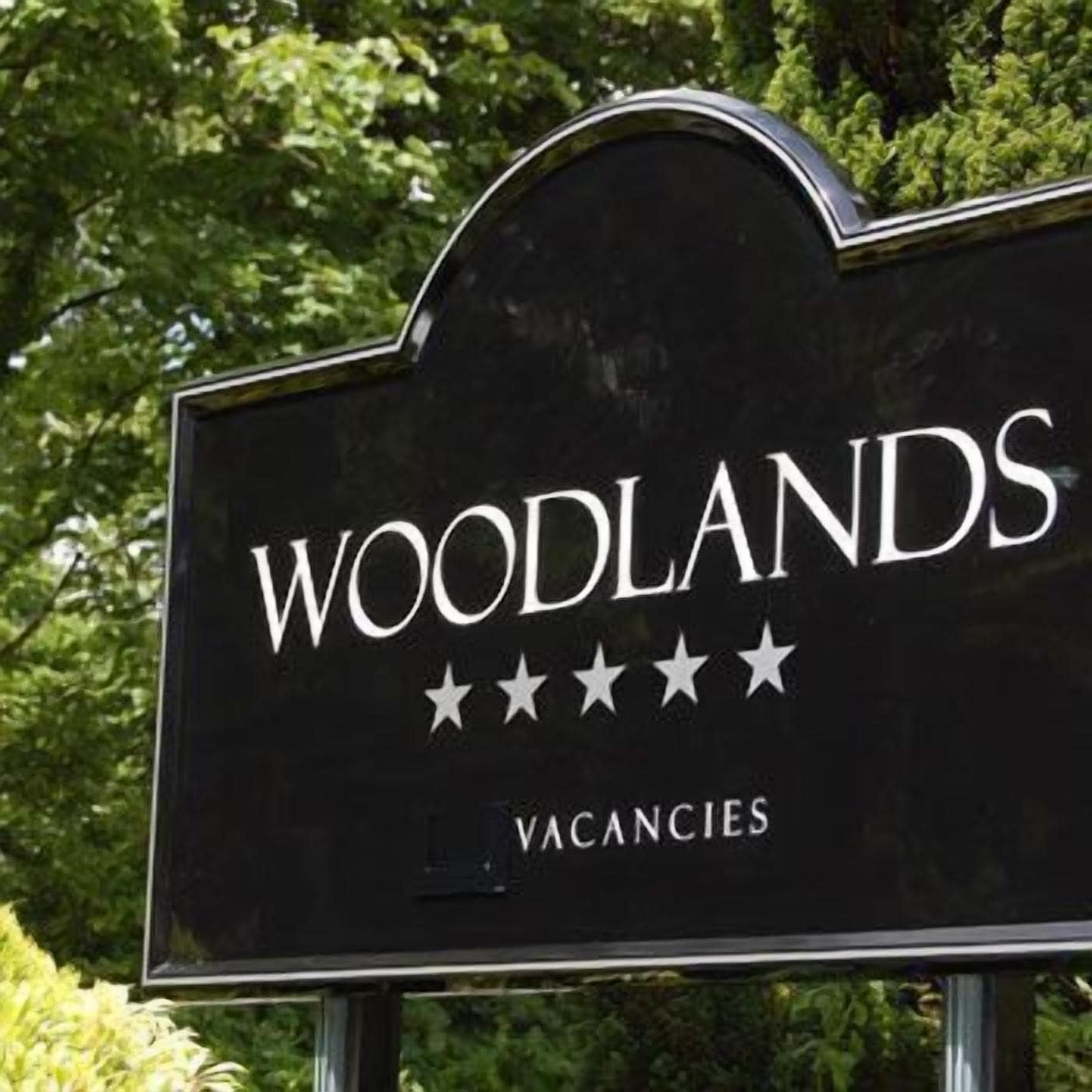 Un letrero con la palabra 'WOODLANDS' y cinco estrellas, que indican una calificación, y la palabra 'VACANCIES' escrita debajo.