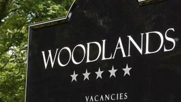 Un letrero con la palabra 'WOODLANDS' y cinco estrellas, que indican una calificación, y la palabra 'VACANCIES' escrita debajo.