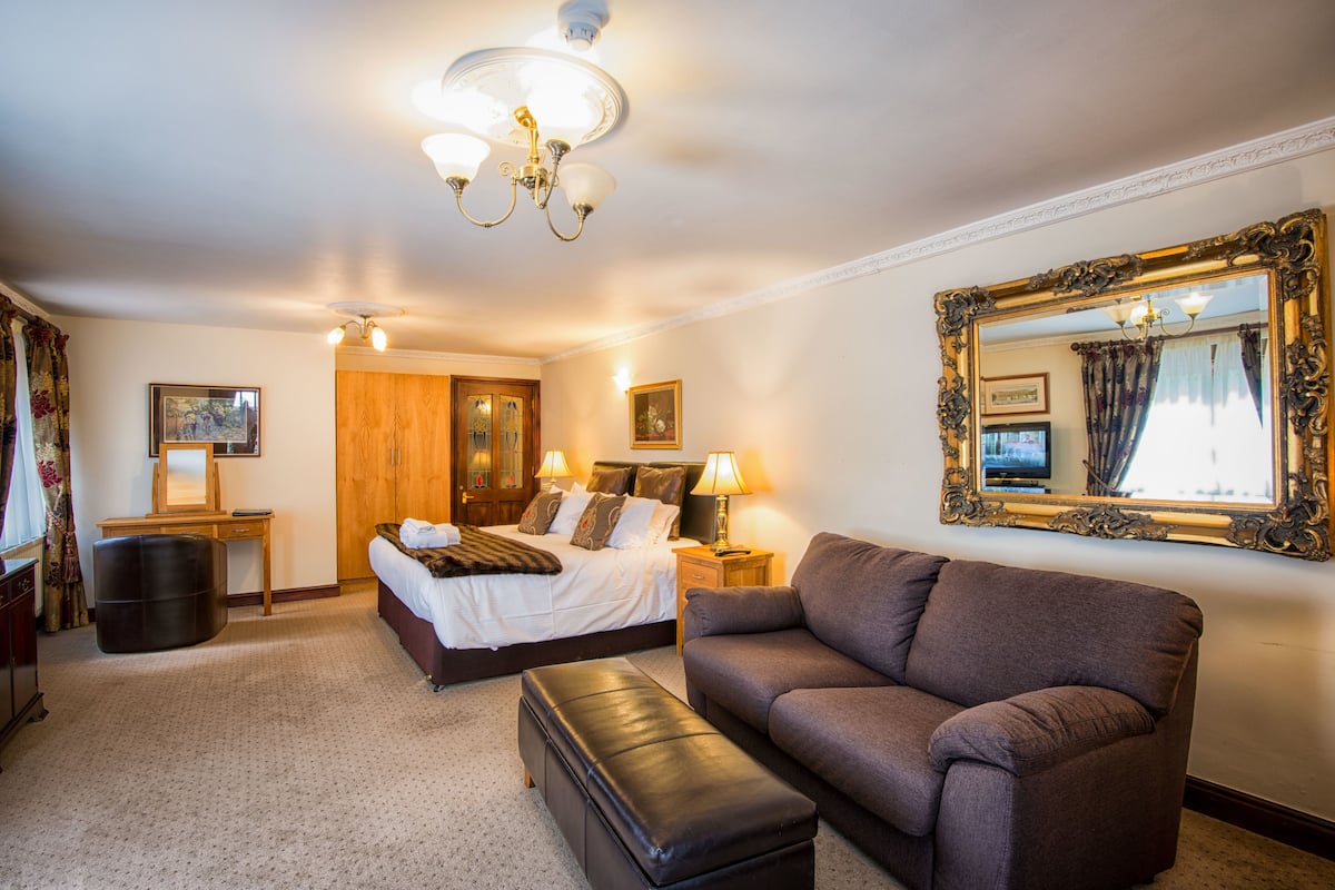 A hotel room with a bed, a sofa, a desk, and a large mirror.
