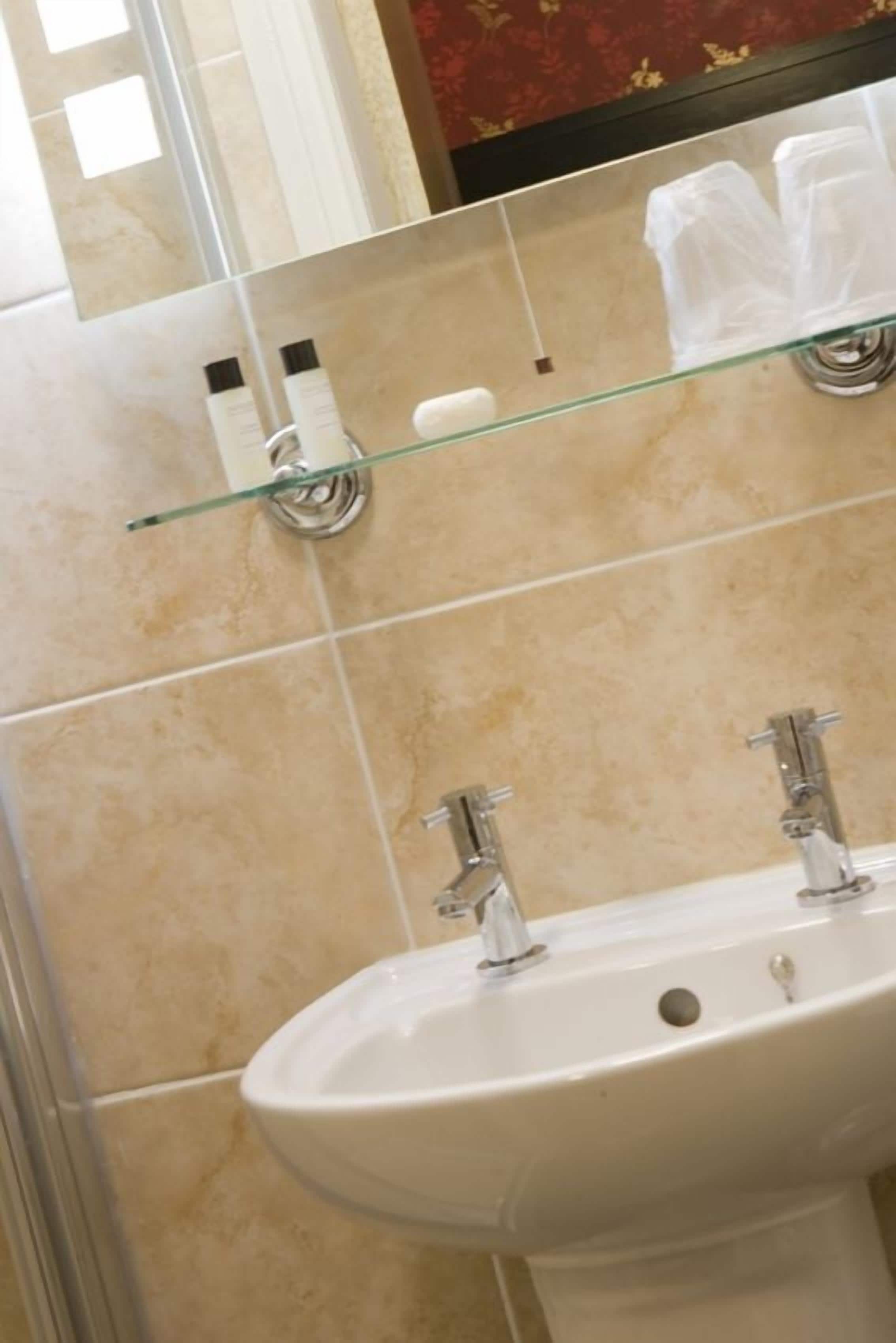A bathroom with a white sink, two faucets, and a glass shelf above the sink.