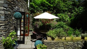A stone building with a wooden door, a white umbrella, and potted plants. - Woodlands Guest House Windermere (Windermere)