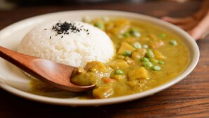 A plate of white rice and a curry dish with peas and chunks of vegetables, served on a wooden table. - The Hostelrie at Goodrich (Ross-on-Wye)