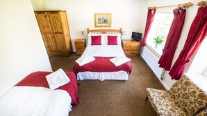 A bedroom with two beds, a wooden wardrobe, a television, and a window with red curtains. - The Hostelrie at Goodrich (Ross-on-Wye)