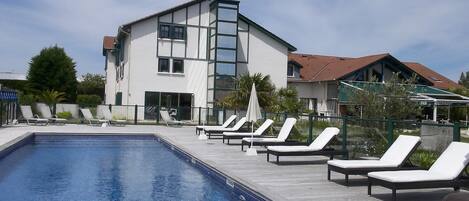 A swimming pool with lounge chairs and a building with large windows in the background.