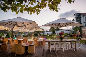 Un patio al aire libre con varias mesas y sillas, sombrillas grandes y plantas en macetas.