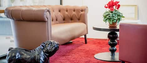 Una habitación con un sofá de cuero capitonado, una mesita redonda con una planta en maceta y una estatua de un perro.