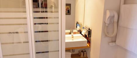 Un baño moderno con cabina de ducha de vidrio, un lavabo con artículos de aseo, un perchero para toallas y un espejo.