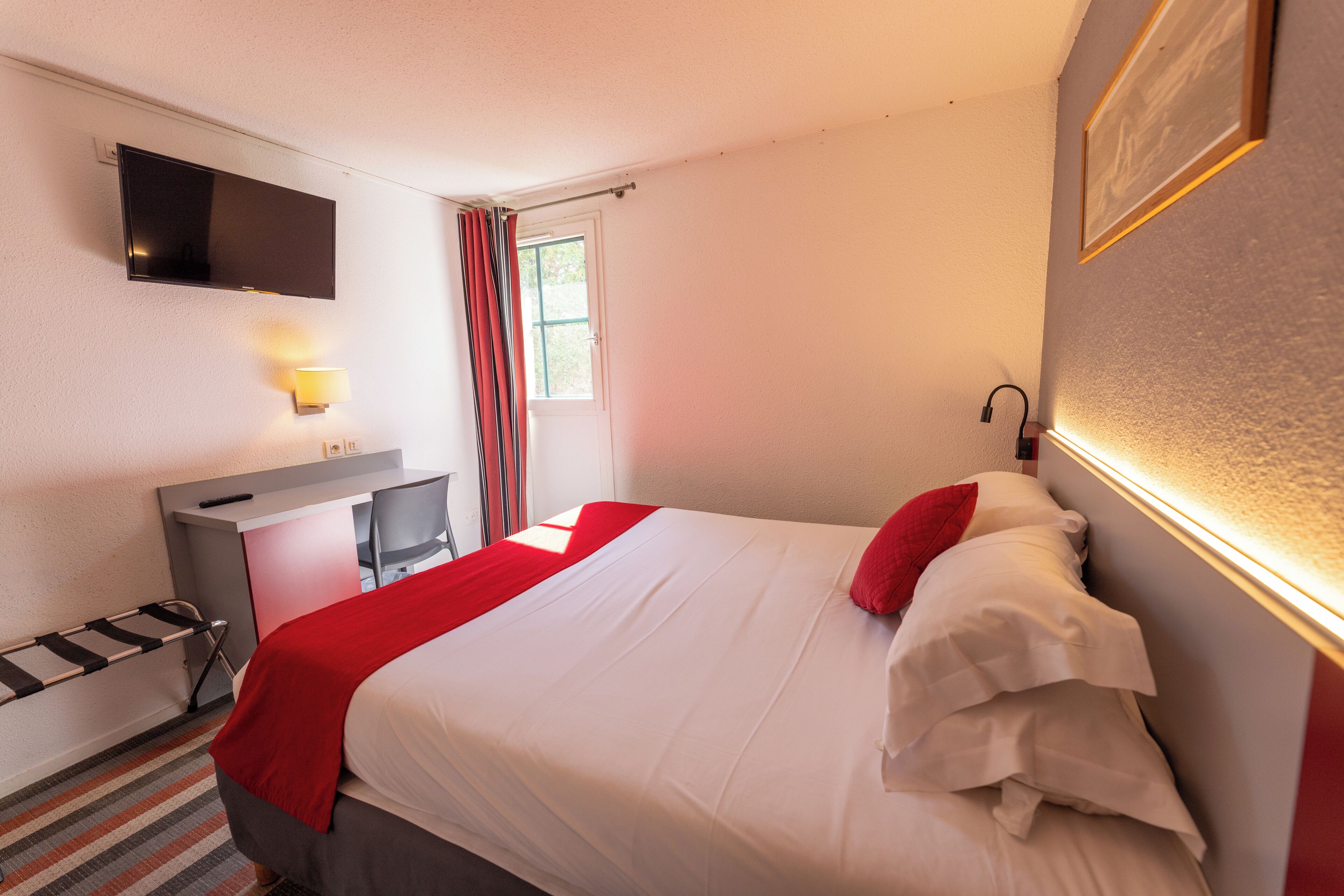 A hotel room with a bed, a desk, a chair, a TV, and a window with curtains.