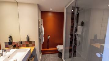 Un baño moderno con un espejo grande, un lavamanos, un inodoro y una zona de ducha con mampara de cristal.