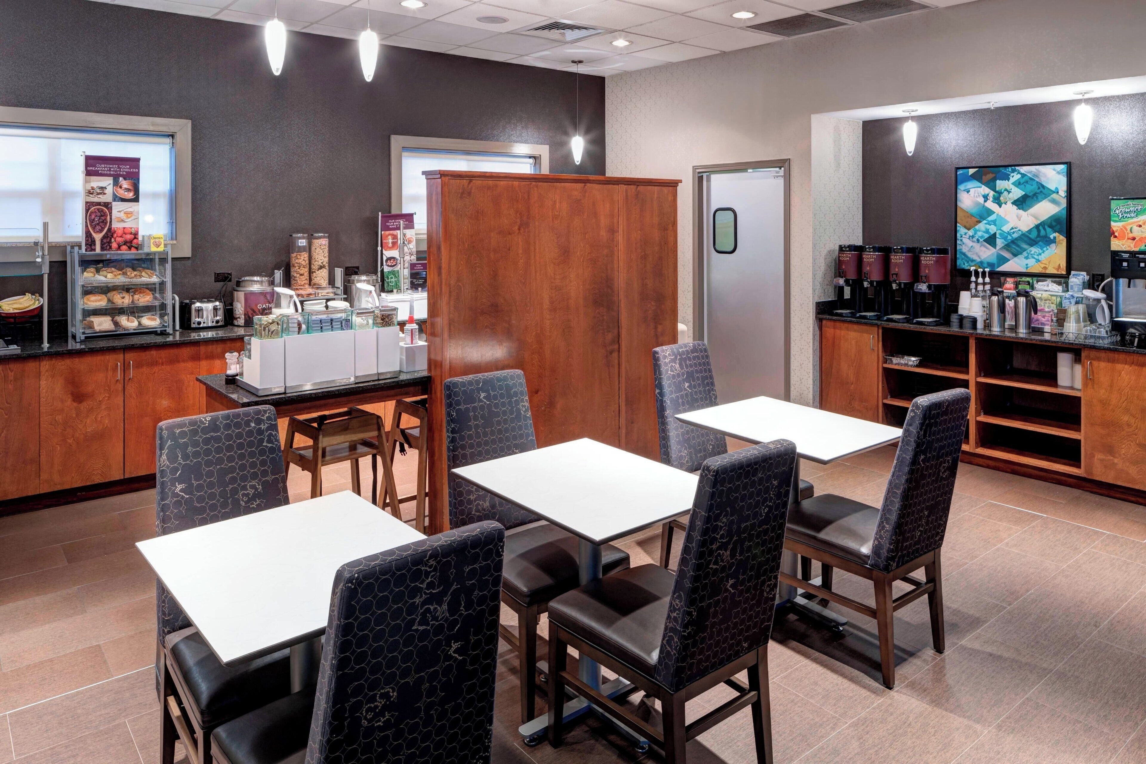 Restaurante com mesas, cadeiras, um espaço para café e um balcão com alimentos.