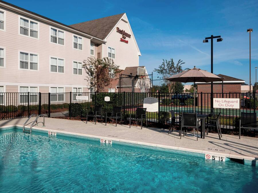 A hotel with a swimming pool, outdoor chairs, and a sign indicating no lifeguard on duty.