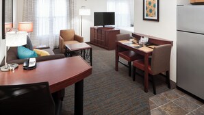 Habitación de hotel con sala de estar, una mesa de comedor, sofá, televisor y refrigerador.