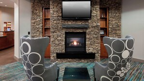 Una sala de estar moderna con pared de piedra, chimenea, televisor de pantalla plana y dos sillones estampados.
