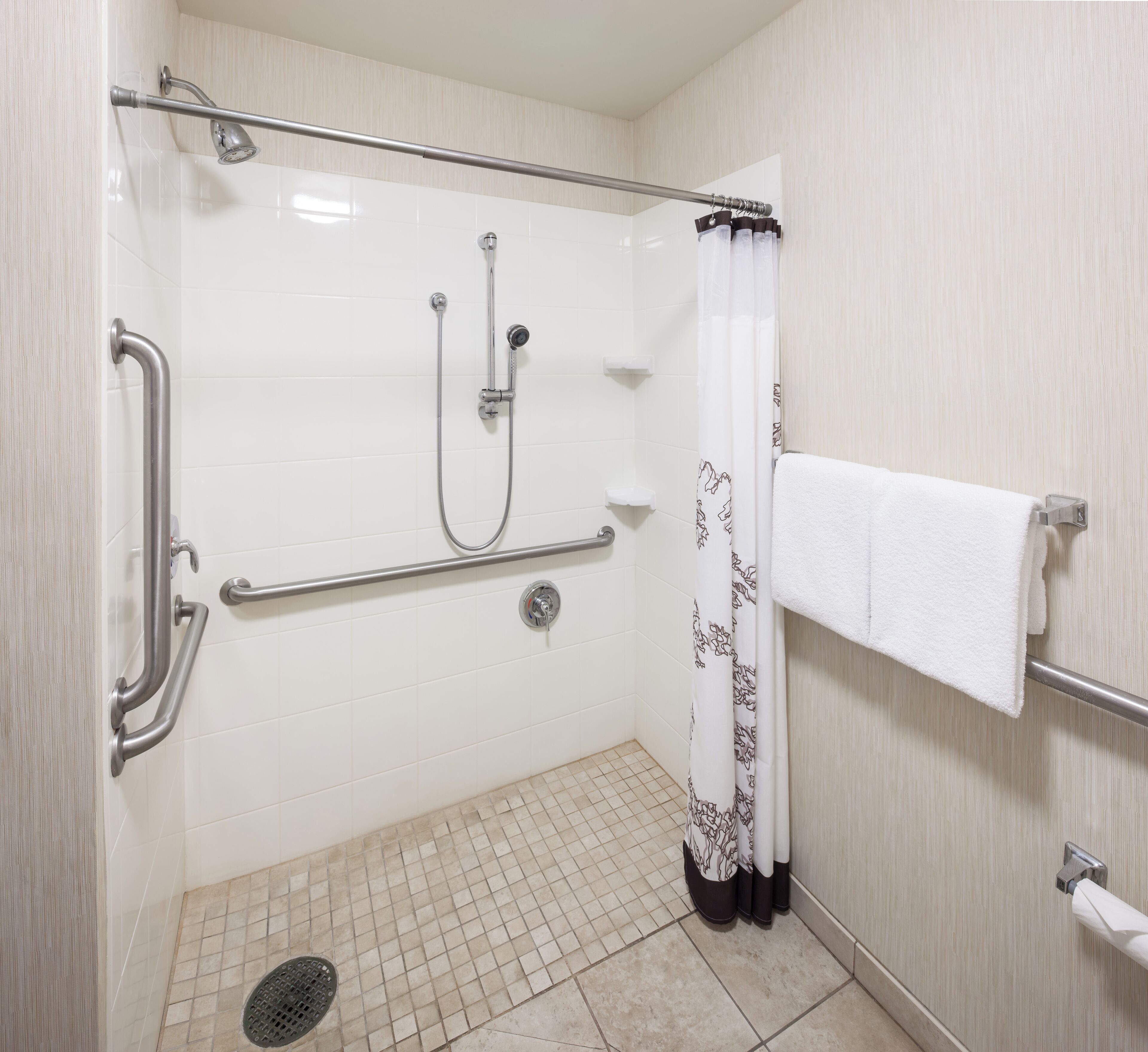 A shower area with a grab bar, a handheld showerhead, and a floor drain.