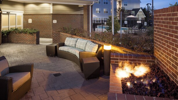 Un patio de hotel con mobiliario exterior, una chimenea y una piscina al fondo.