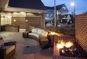 A hotel patio with outdoor seating, a fire feature, and a pool in the background.