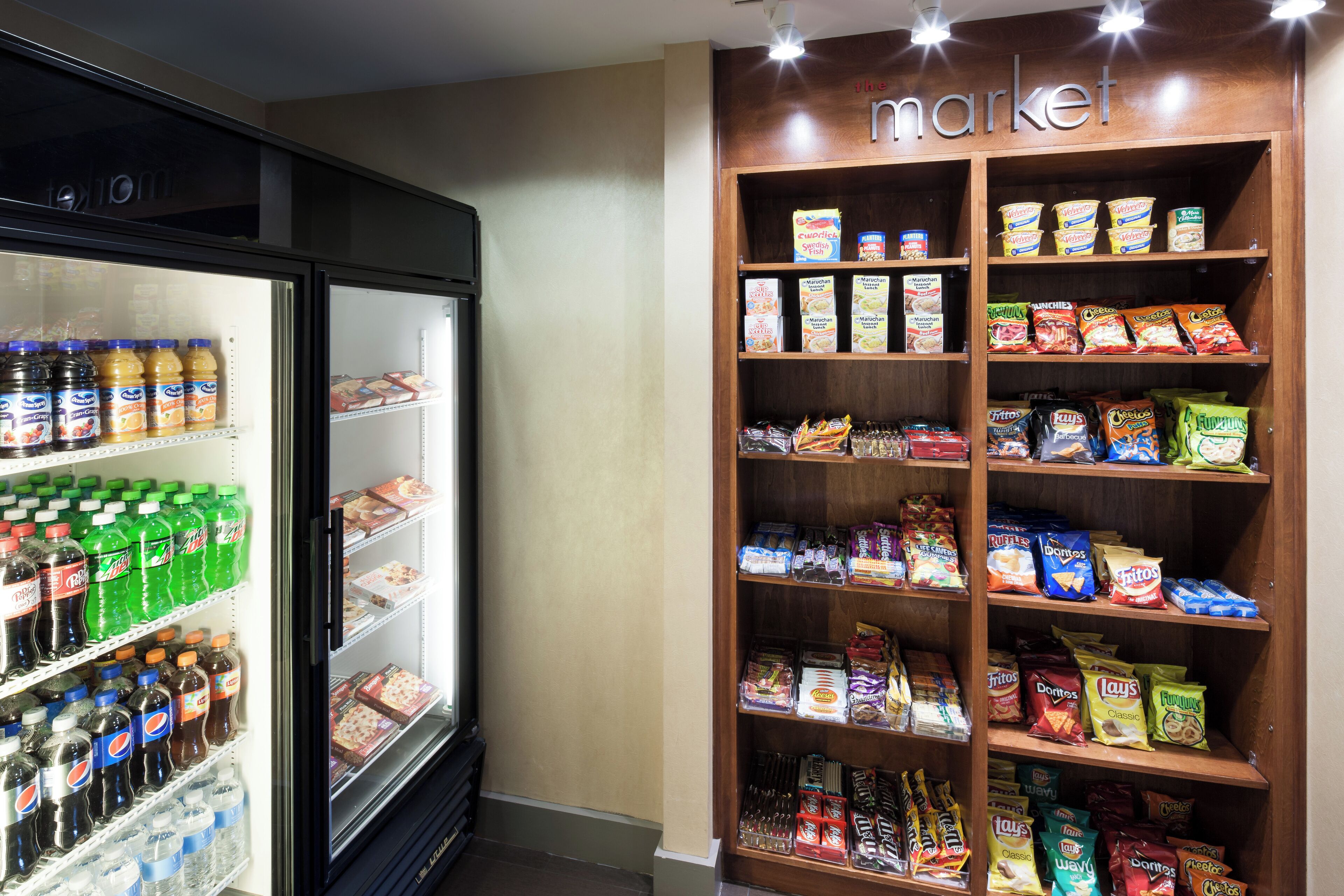 A grocery store with a refrigerated section on the left and a shelf stocked with snacks and cereals on the right.